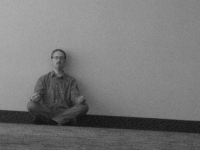 Black and white photo of man sitting on floor, meditating.