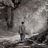 A black and white photo of a monk walking on a path in the forest.