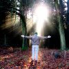 Man standing in the forest, with hand opening out welcoming light from the sun.