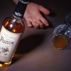 An alcohol bottle with the label Poison and a wine glass with some alcohol inside, a hand in the background.