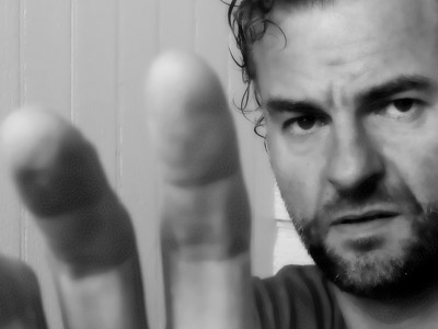 A man with a serious face, not smiling and using his hand trying to cover part of the photo.