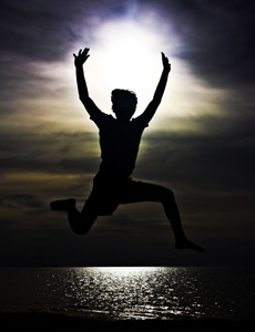 A boy jumping very high up at a beach.