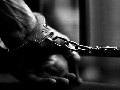 An arm handcuffed to prison bars.