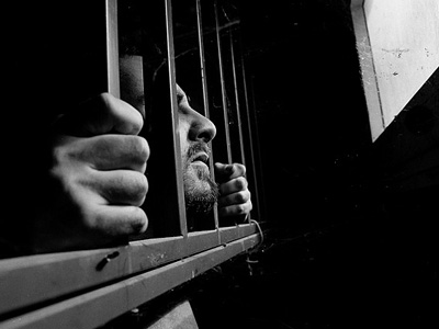 Black and white photo of a man looking out of jail cell.