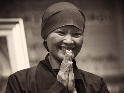A nun smiling with palms together.