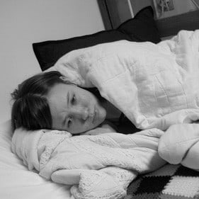 Photo of woman lying in bed, looking sad.