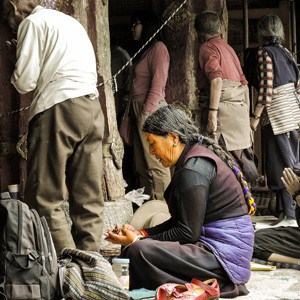 An old woman sitting on the floor chanting with the mala on her hand.