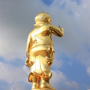 The back view of a golden statute of the young shakyamuni Buddha, pointing in the sky.