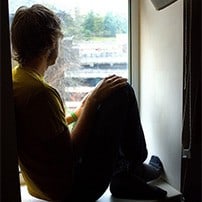 Young man sitting on window sill, staring out window.