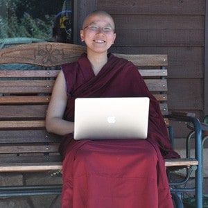 Venerable Damcho, sitting outside, working on a laptop and smiling.