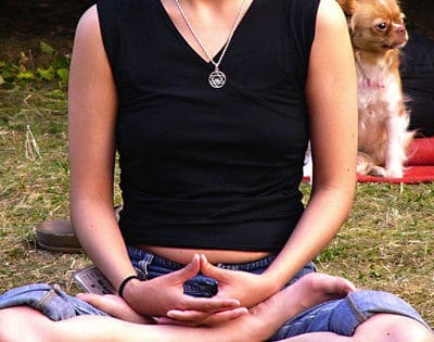 Person meditating outside with dog in background.