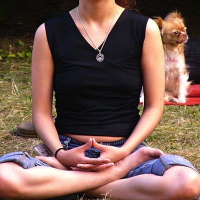 Person meditating outside with dog in background.