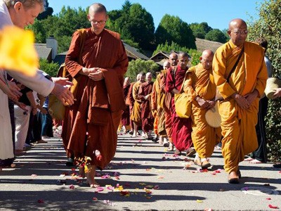 Bhikshuni and bhikshunis walking in 2 rows, with lay person spreading flowers on the path.