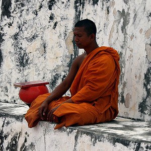 Thai monk sitting outside next to alms bowl, meditating.