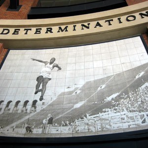 The words: Determination above a big screen, screen showing a woman doing a long jump.