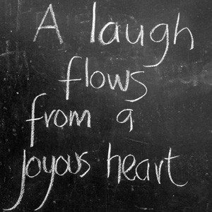 The words: A laugh flows from a joyous heart, written on a blackboard.