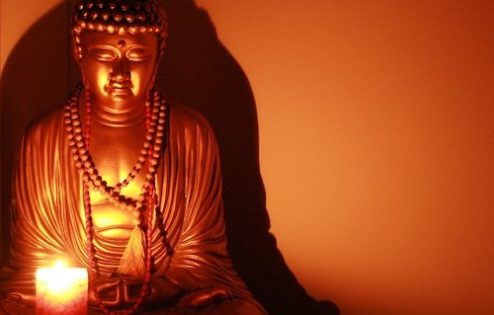 Statute of a buddha and a candle light shining in front of the buddha.
