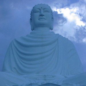 Large Buddha statue against blue sky with clouds.