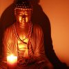 Statute of a buddha and a candle light shining in front of the buddha.