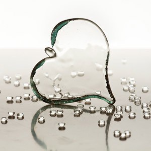 A glass heart and with glass tears on a reflective surface.