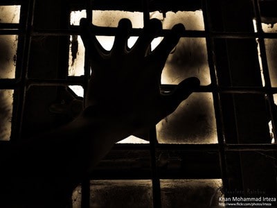 A hand gripping at the window grills in a dark place.