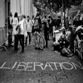 People walking on the street, the words Liberation on the floor of the street.