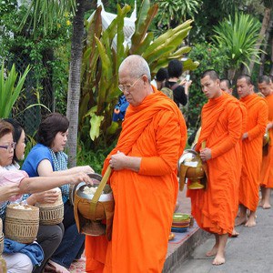 An elderly monk receiving alms, other young monks lining at the back.