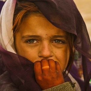 An Afghan girl's face full of emotion, using her sunburnt hand to cover her mouth.