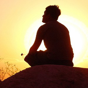Silhouette of man metitating in front of sunrise.