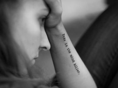 A woman putting her hand on her forehead, the words: Fear is the mind killer on her arm.