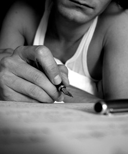 A man wearing a singlet using a fountain pen to write a letter.