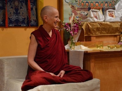 Czcigodny Thubten Chodron siedzący w pozycji medytacyjnej i uśmiechający się radośnie.
