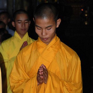 Young monk with palms together and head bowed.