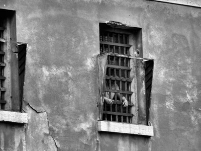 Um homem parado em uma janela de grade altamente prisional.