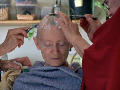 Venerable Samten with eyes closed while two nuns shave her head.