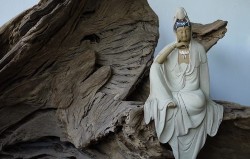 Una estatua de Kuan Yin en contemplación sentada sobre un trozo de corteza de madera.