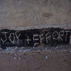Betonowa ściana ze słowem: Radość + Wysiłek