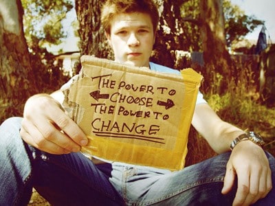 A guy sitting down on grass, his hand holding a cardboard with the words: The power to choose The power to change.