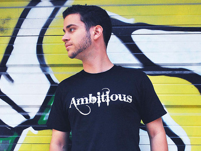 Młody mężczyzna ubrany w czarną koszulkę z napisem „Ambitious”.