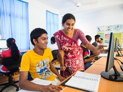 Young woman smiling, helping a young man on the computer.