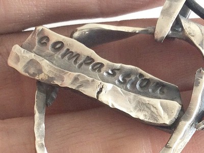 The word 'compassion' engraved into silver metal.