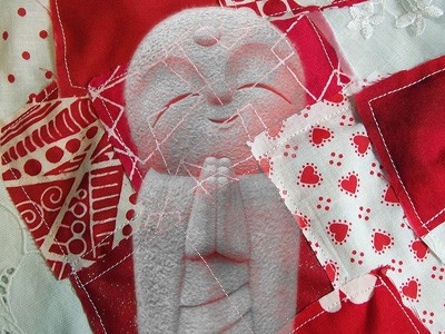 Jizo over a red and white patchwork quilt.