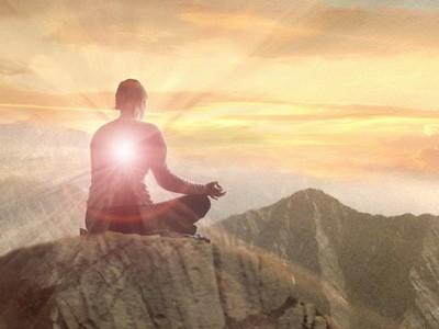 Osoba siedząca na szczycie góry, medytująca.