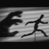 Shadow of a hand trying to catch a shadow of a man running away.
