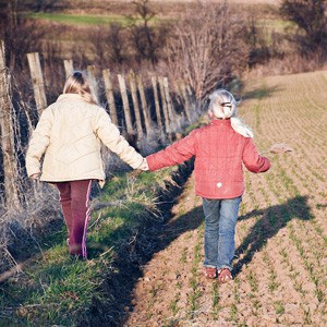 2 young girls holding hands together, walking in a field.
