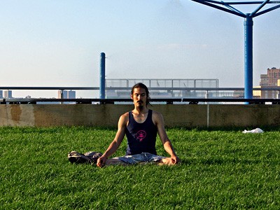 Mężczyzna siedzący na zewnątrz w trawie, medytujący.