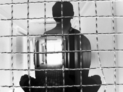 Transparent silhouette of man meditating behind prison bars.