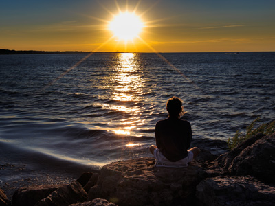 A woman meditating on a rock by the seaside during sunset.