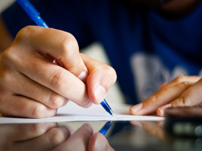 A hand holding a pen, writing on a piece of paper.