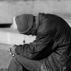 A sad man sitting in the street, head bowing low.